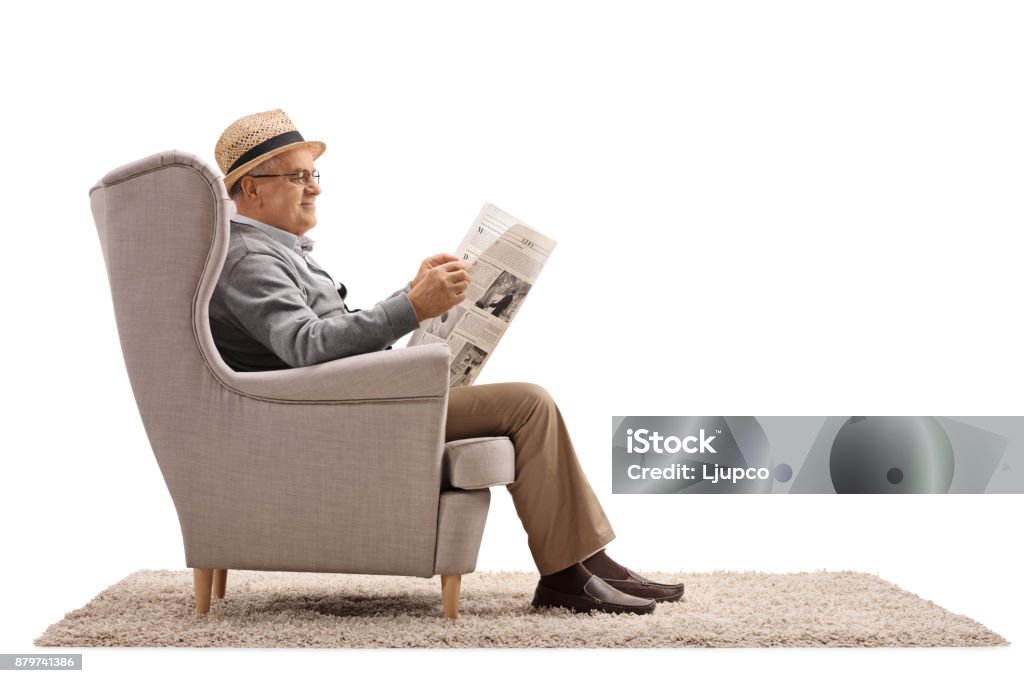 Mature man sitting in an armchair and reading a newspaper Mature man sitting in an armchair and reading a newspaper isolated on white background Chair Stock Photo