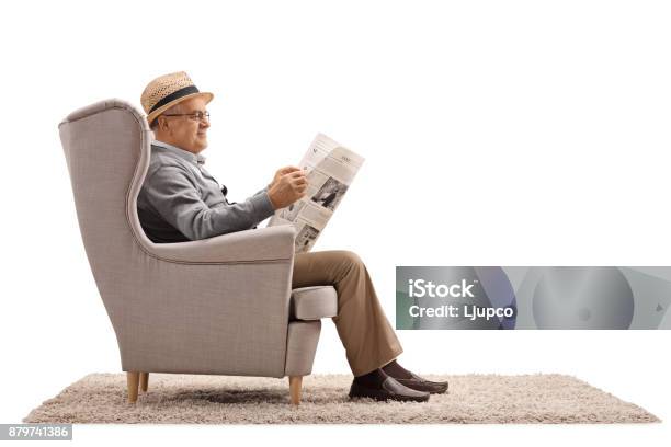 Mature Man Sitting In An Armchair And Reading A Newspaper Stock Photo - Download Image Now