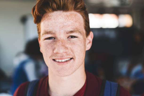 Close-up of smiling redhead teenage boy Close-up of smiling redhead teenage boy. Portrait of male student is standing in classroom. He is with freckles. 16 17 years stock pictures, royalty-free photos & images