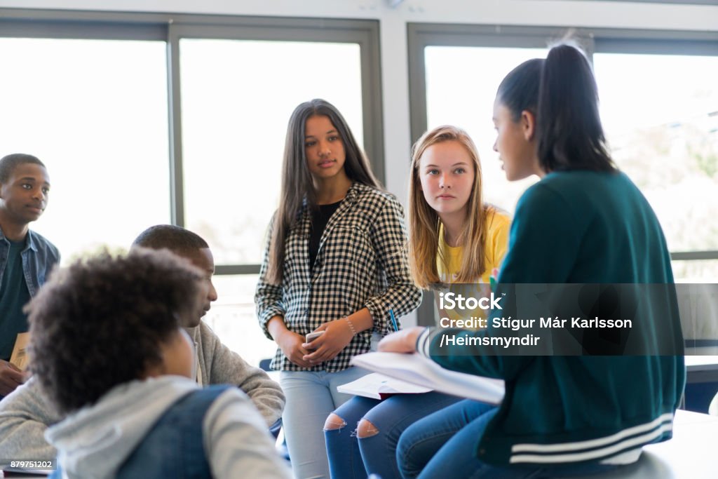Multi-ethnic students discussing in classroom High school students are discussing against window. Multi-ethnic male and females are in classroom. They are wearing casuals at school. Teenager Stock Photo
