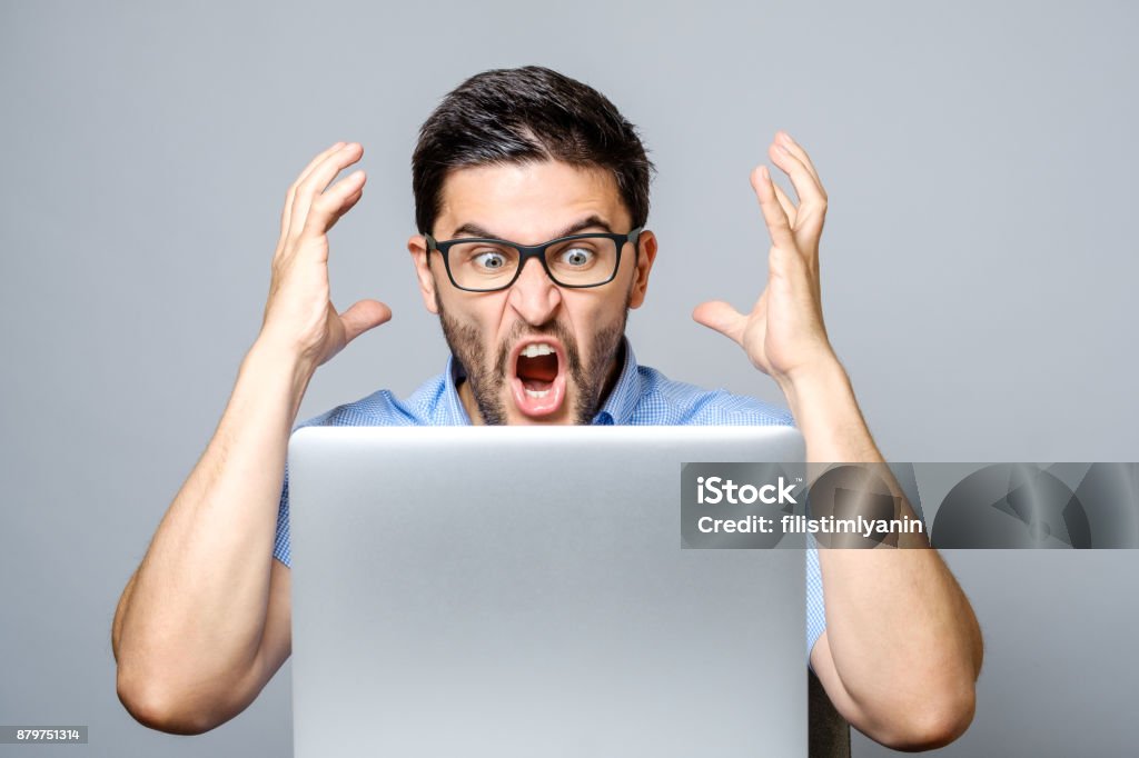 Portret van verbaasd man met laptopcomputer via grijze achtergrond - Royalty-free Woede Stockfoto