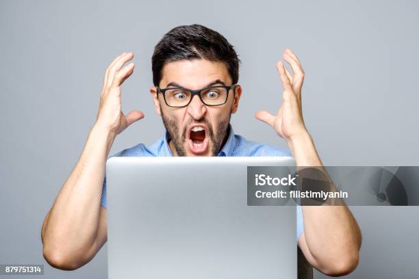 Portret Van Verbaasd Man Met Laptopcomputer Via Grijze Achtergrond Stockfoto en meer beelden van Woede