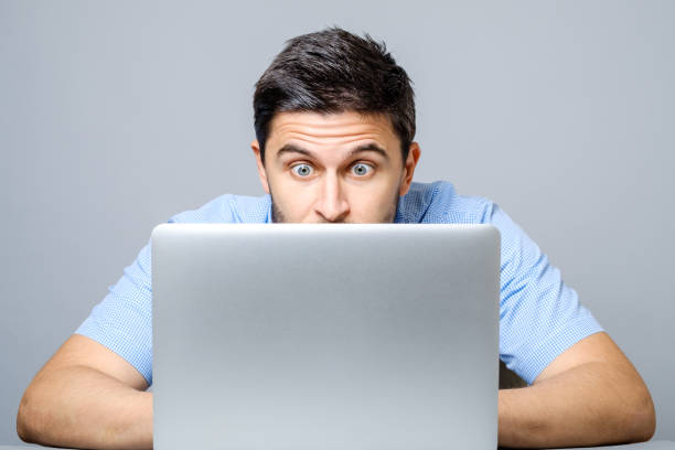 istock Young shocked man dressed in blue shirt while using laptop. Isolated on gray 879751324