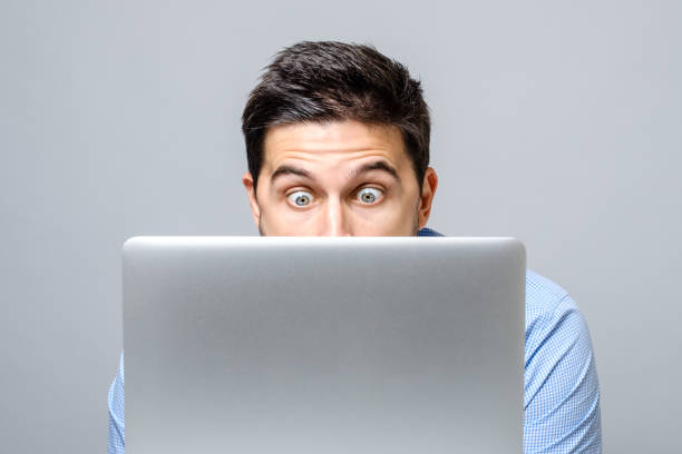 istock Young shocked man dressed in blue shirt while using laptop. Isolated on gray 879751352