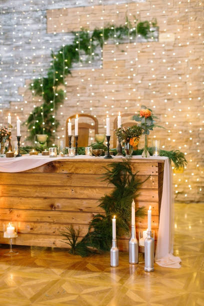 istock illumination, party space, wealth concept. extremelly bright chamber illuminated with lots of twinkle lights and burning candles, wooden table surved for newlyweds with fresh branches of pine 879754230