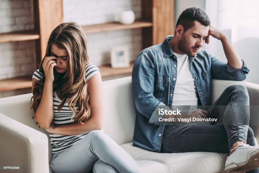 Upset couple at home. Upset couple at home. Handsome man and beautiful young woman are having quarrel. Sitting on sofa together. Family problems. Couple - Relationship Stock Photo