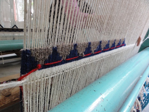 Woman hands weaving threads at a loom.