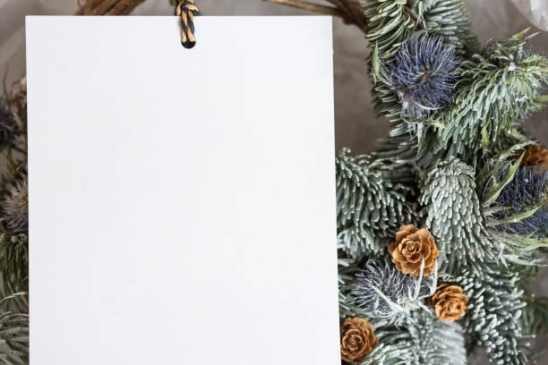 istock invitation, polygraphy, winter holidays concept. there is negative space for text on the white card on the thin rope, it is applied to conifer wreath richly embellished with pinecones and burdock 879770030