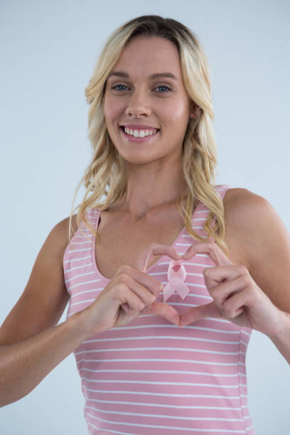 istock Smiling woman making heart shape on pink ribbon 879781146