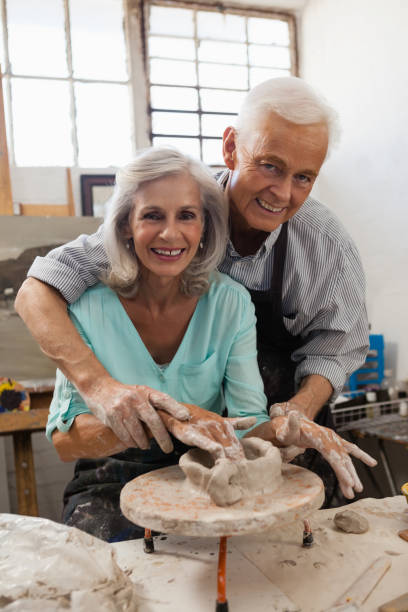 istock Smiling senior man assisting senior woman in making pottery during drawing class 879798150