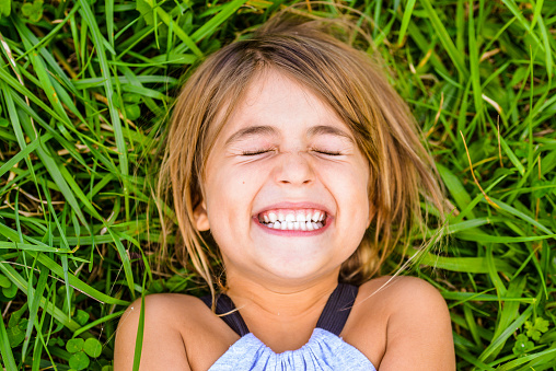Happy, smiling, laughing little girl lays in a field of grass. Full of happiness and joy