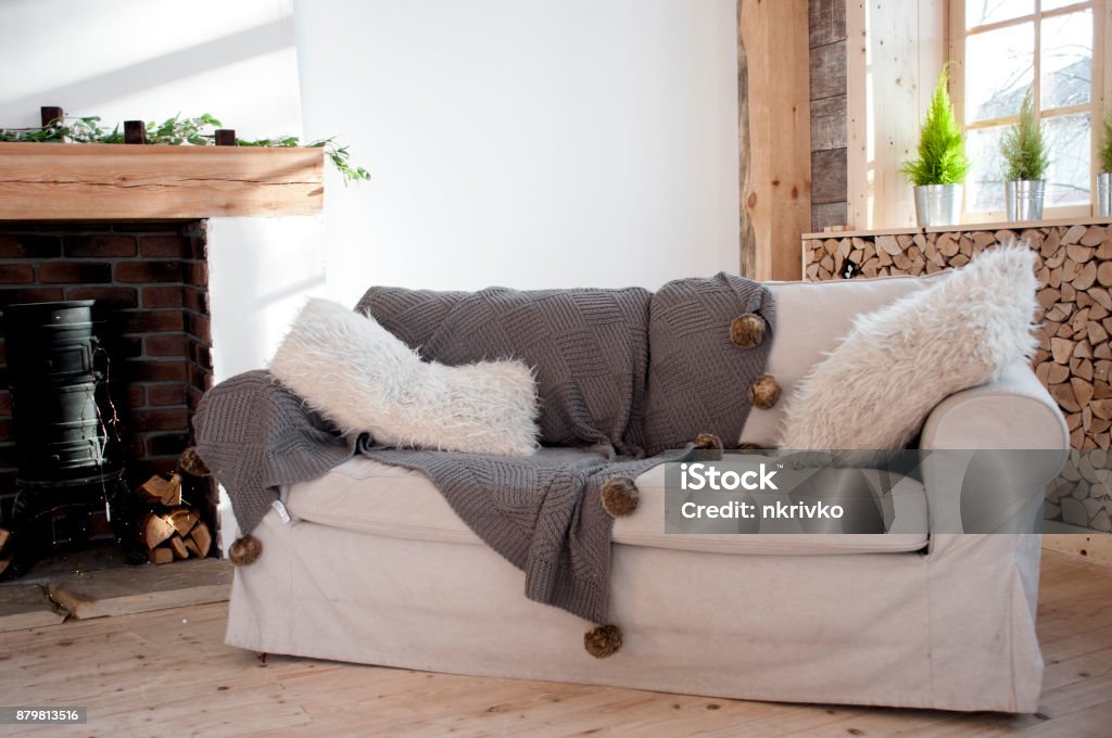 White Sofa With Fluffy Pillows And A Coverlet With Pompoms Near The  Fireplace Stock Photo - Download Image Now - iStock