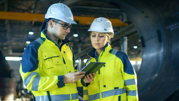 istock Male and Female Industrial Engineers in Hard Hats Discuss New Project while Using Tablet Computer. They're Making Calculated Engineering Decisions.They Work at the Heavy Industry Manufacturing Factory. 879813698