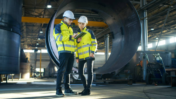 istock Male and Female Industrial Engineers in Hard Hats Discuss New Project while Using Tablet Computer. They're Making Calculated Engineering Decisions.They Work at the Heavy Industry Manufacturing Factory. 879813702