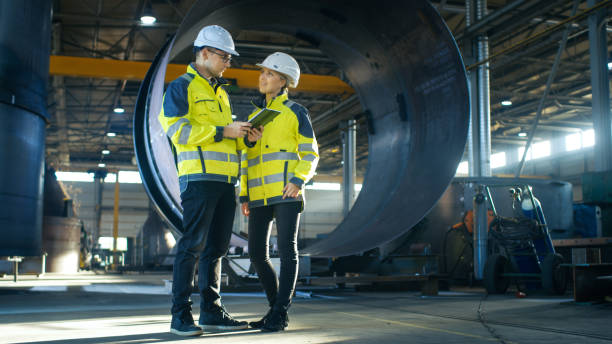 istock Male and Female Industrial Engineers in Hard Hats Discuss New Project while Using Tablet Computer. They're Making Calculated Engineering Decisions.They Work at the Heavy Industry Manufacturing Factory. 879813730