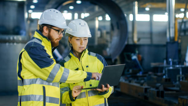 masculino y femenino ingenieros industriales en duro sombreros discutir su nuevo proyecto al uso del ordenador portátil. hacen mostrando gestures.they trabajo en una industria pesada fábrica. - ingeniera fotografías e imágenes de stock