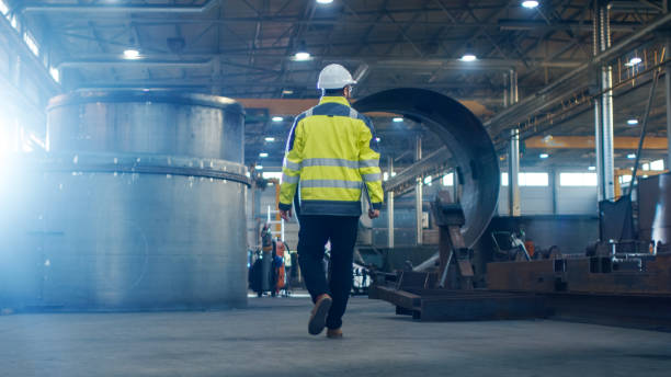 istock Industrial Engineer in Hard Hat Wearing Safety Jacket Walks Through Heavy Industry Manufacturing Factory with Various Metalworking Processes. 879813872