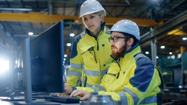 istock Male Industrial Engineer Works on the Personal Computer while Female Manager Talks about Project. They Work in Heavy Industry Manufacturing Factory. 879814010