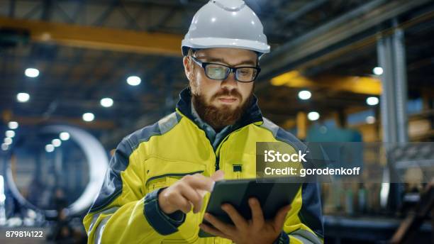 安全ジャケットを身に着けているヘルメットの工業エンジニアはタッチ スクリーン タブレット コンピューターを使用します彼は重工業の製造工場で働いています - テクノロジーのストックフォトや画像を多数ご用意