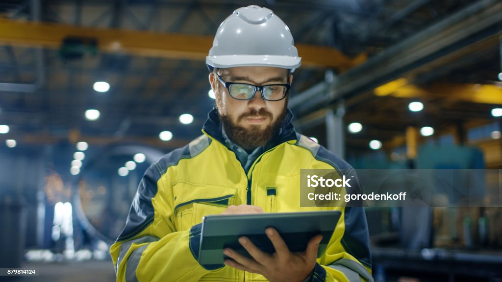 Ingeniero industrial en casco, con chaqueta de seguridad utiliza pantalla táctil Tablet PC. Trabaja en la industria pesada fábrica. - Foto de stock de Ingeniero libre de derechos