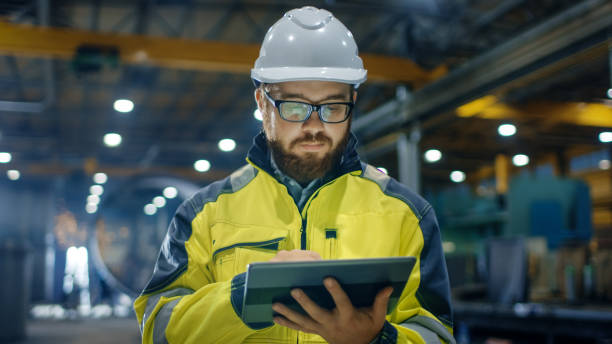 istock Industrial Engineer in Hard Hat Wearing Safety Jacket Uses Touchscreen Tablet Computer. He Works at the Heavy Industry Manufacturing Factory. 879814124