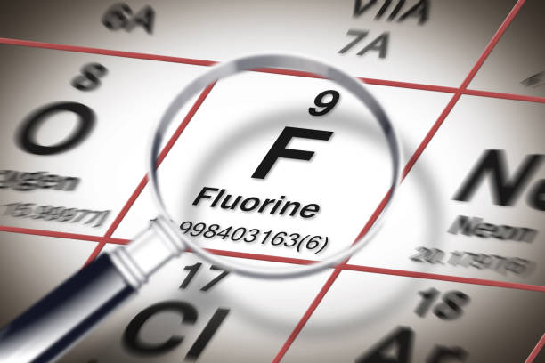 focus on fluorine chemical element - element against tooth decay - concept image with a magnifying glass above the mendeleev periodic table - mendeleev table imagens e fotografias de stock
