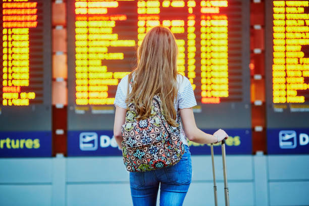 Tourist girl with backpack in international airport Beautiful young tourist girl with backpack and carry on luggage in international airport, near flight information board cancelled stock pictures, royalty-free photos & images