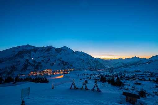 austrian alpine ski resort obertauern in twilight blue hour snow covered mountains and ski slopes after sunset town lit skiers skiing down after apres-ski wide shot