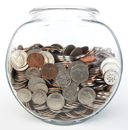 Front view of glass fish bowl filled with United States coins. Savings concept. Isolated.