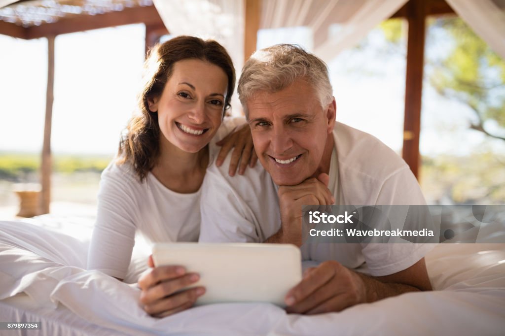 Portrait of happy couple using digital tablet on bed Portrait of happy couple using digital tablet on bed during morning 55-59 Years Stock Photo