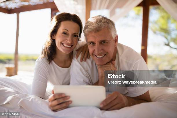 Portrait Of Happy Couple Using Digital Tablet On Bed Stock Photo - Download Image Now