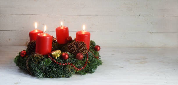 adventskranz mit vier roten brennenden kerzen und weihnachtsdekoration auf rustikale weiße holz, panoramaformat mit textfreiraum - adventskranz stock-fotos und bilder