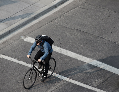 A male bike messenger rides his bike on a city street on his way to make a delivery. He is riding a one speed or fixed gear road bike.