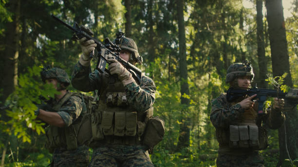 istock Three Fully Equipped Soldiers Wearing Camouflage Uniform Attacking Enemy, They're in Shooting Ready Stance, Aiming Rifles. Military Operation in Action, Squad Standing in Dense Forest. 879912974