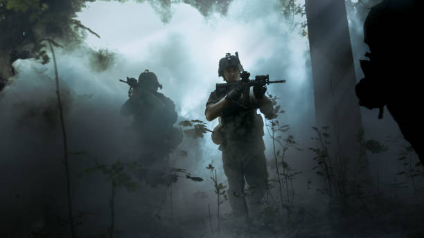 istock Fully Equipped Soldiers Wearing Camouflage Uniform Attacking Enemy, Rifles Ready to Shoot. Military Operation in Action, Squad Running in Formation Through Cold Dense Smokey Forest. 879912990