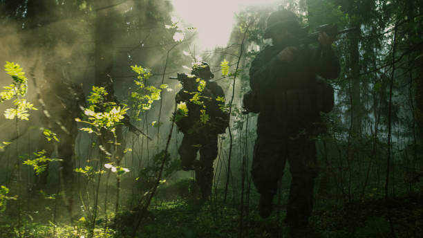 istock Fully Equipped Soldiers Wearing Camouflage Uniform Attacking Enemy, Rifles Ready to Shoot. Military Operation in Action, Squad Running in Formation Through Dense Smokey Forest. 879913024