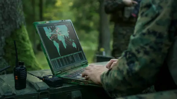 Photo of Military Operation in Action, Soldiers Using Military Grade Laptop Targeting Enemy with Satellite. In the Background Camouflaged Tent on the Forest.