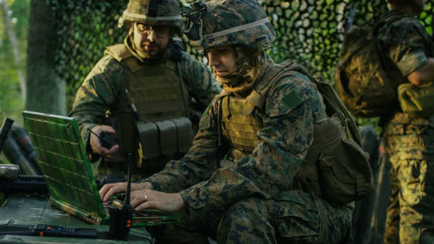 Military Staging Base, Officer Gives Orders to Chief Engineer, They Use Radio and Army Grade Laptop. They're in Camouflaged Tent in a Forest. They're on Reconnaissance Operation/ Mission. Military Staging Base, Officer Gives Orders to Chief Engineer, They Use Radio and Army Grade Laptop. They're in Camouflaged Tent in a Forest. They're on Reconnaissance Operation/ Mission. afghanistan army stock pictures, royalty-free photos & images