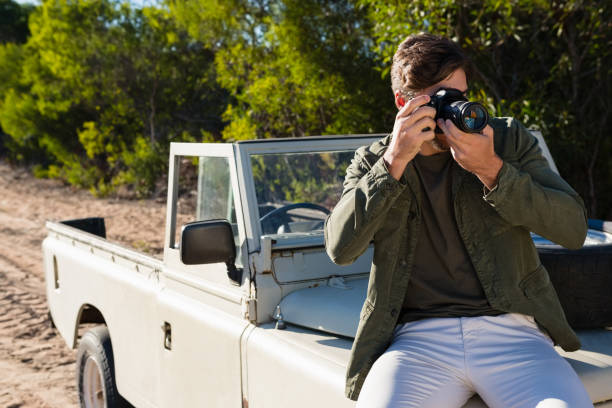 istock Man photographing while sitting on vehicle hood 879947054