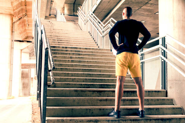Rearview of a man standing with his hands on his hips at the bottom of a set of stairs while out for a city run. Sport, fitness and healthy lifestyle concept