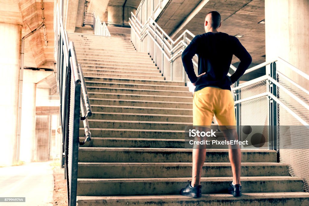 Young sport man preparing for a challenge in urban environment. Rearview of a man standing with his hands on his hips at the bottom of a set of stairs while out for a city run. Sport, fitness and healthy lifestyle concept Challenge Stock Photo