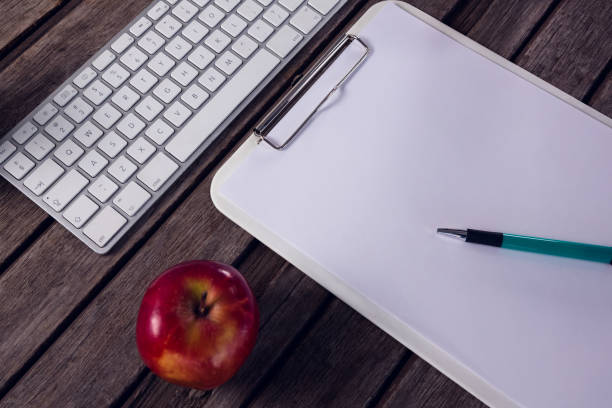 istock Keyboard, clipboard, apple and pen on wooden table 879973602