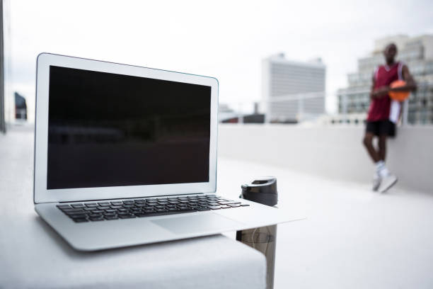 Close-up of laptop on table with football player standing in background