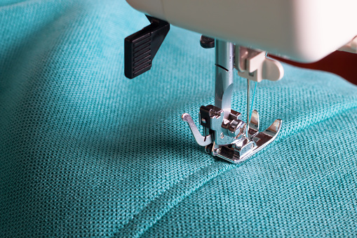 Close up of sewing machine working with turquoise fabric