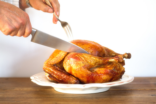 Man's Hands Carving Turkey on Platter on Antique Wood Table, White Background