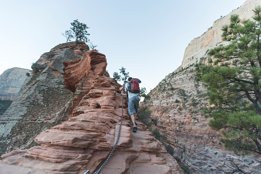 A young male backpacker carefully holds a safety line as he climbs up a boulder in a magnificent rock canyon. The shot is from low and behind.