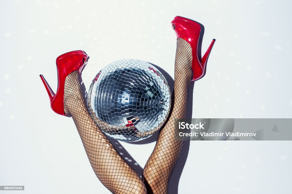 Woman in red heels and disco ball Direct flash detail of woman in red dress, heels, disco ball and champagne bottle lying down on floor. Nightclub Stock Photo