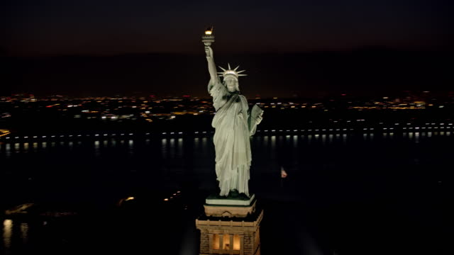 AERIAL Statue of Liberty shining in the night with Lower Manhattan seen in the background