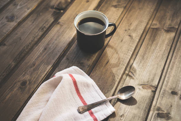 White ceramic cup of black coffee on a saucer with a small spoon on a black background. Close-up.