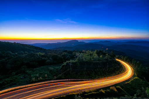 Sunrise scence of car light trail to the top with curve of road at Doi Inthanon National park in Chiang Mai Province, Thailand.